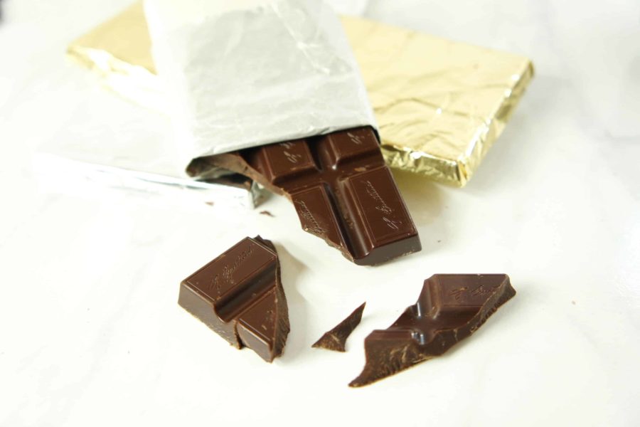 A chocolate bar with broken pieces scattered around it on a white table