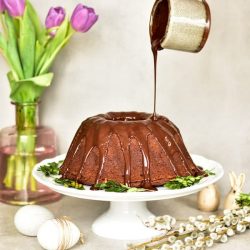 bundt cake with chocolate glaze being poured over it on a white cake stand