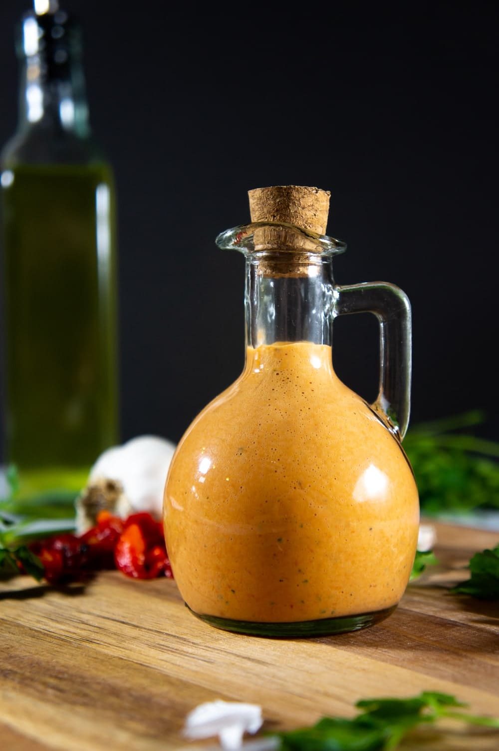 A jar of red pepper aioli on a wooden cutting board with parsley leaves