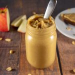 a jar of peanut butter in front of a sliced apple and plate