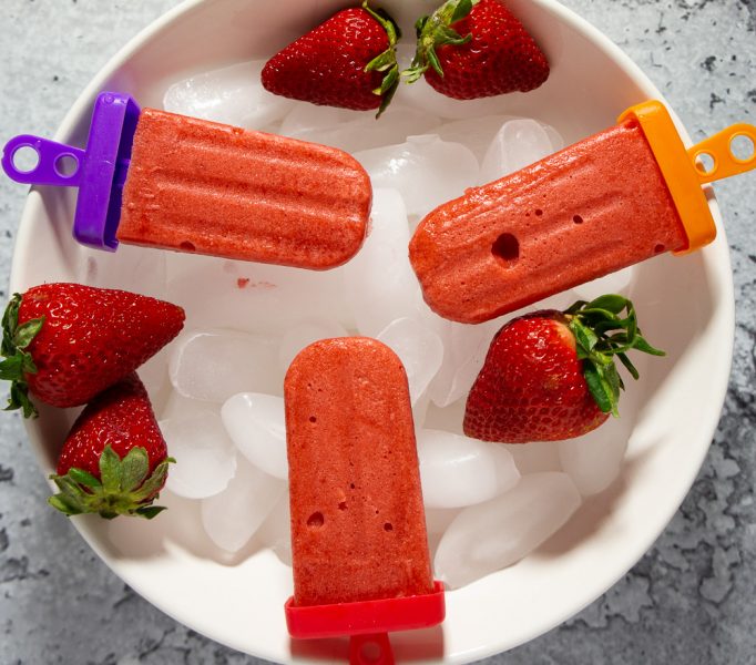 three strawberry sorbet popsicles on a bed of ice