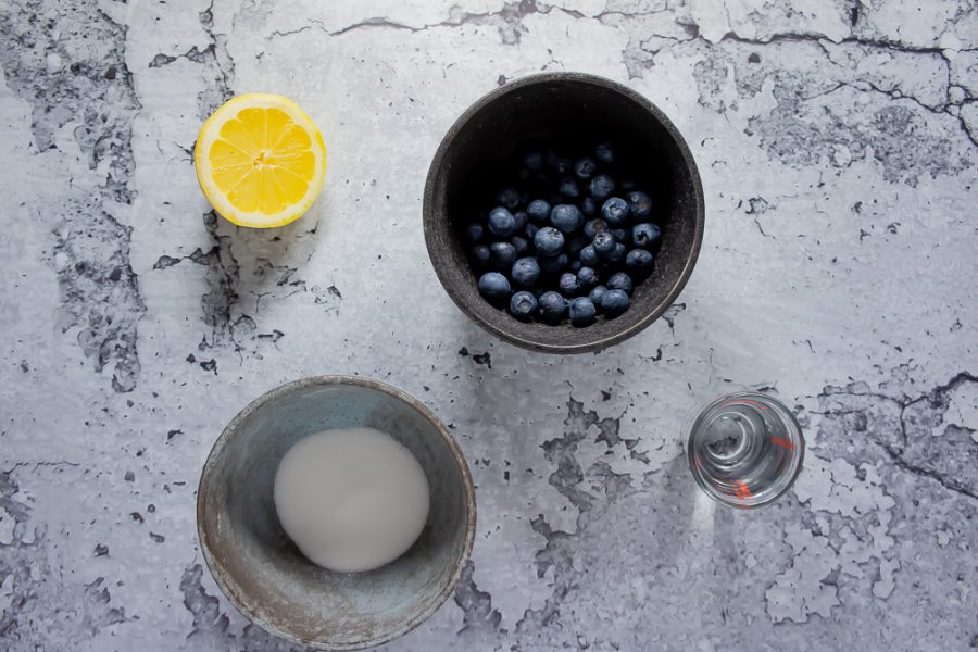 a bowl of blueberries, half a lemon, sugar, and water