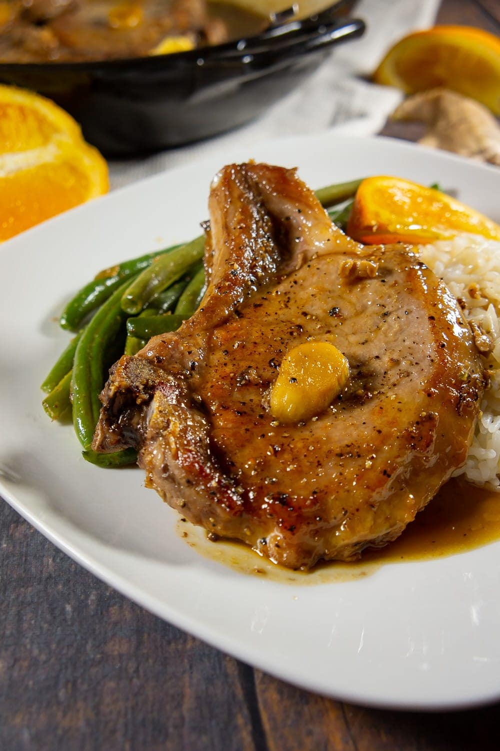 a white plate with pork chops, green beans, rice, and a slice of orange