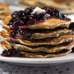 a stack of buckwheat pancakes topped with blueberry compote.