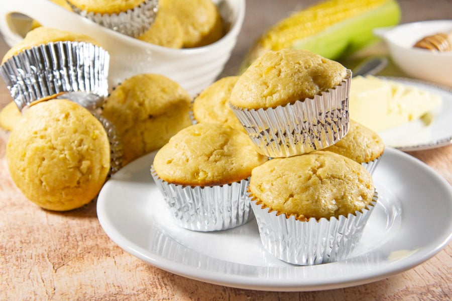 plate of cornbread muffins in front of a fresh corn on the cob and a bowl