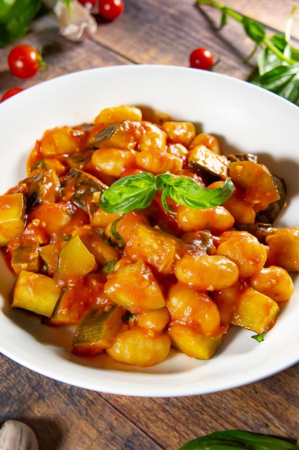 white bowl with gnocchi in tomato sauce and basil inside on a wooden table