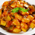 close up of a red sauce on gnocchi with zucchini and basil