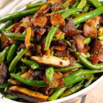 an oval bowl of green beans with mushrooms and onions