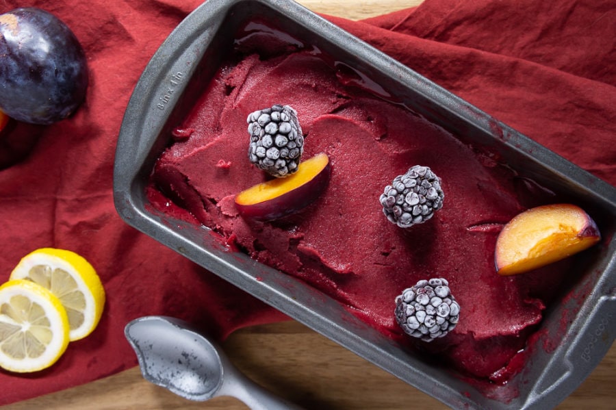 metal loaf pan full of plum blackberry sorbet topped with frozen berries and slices of plums