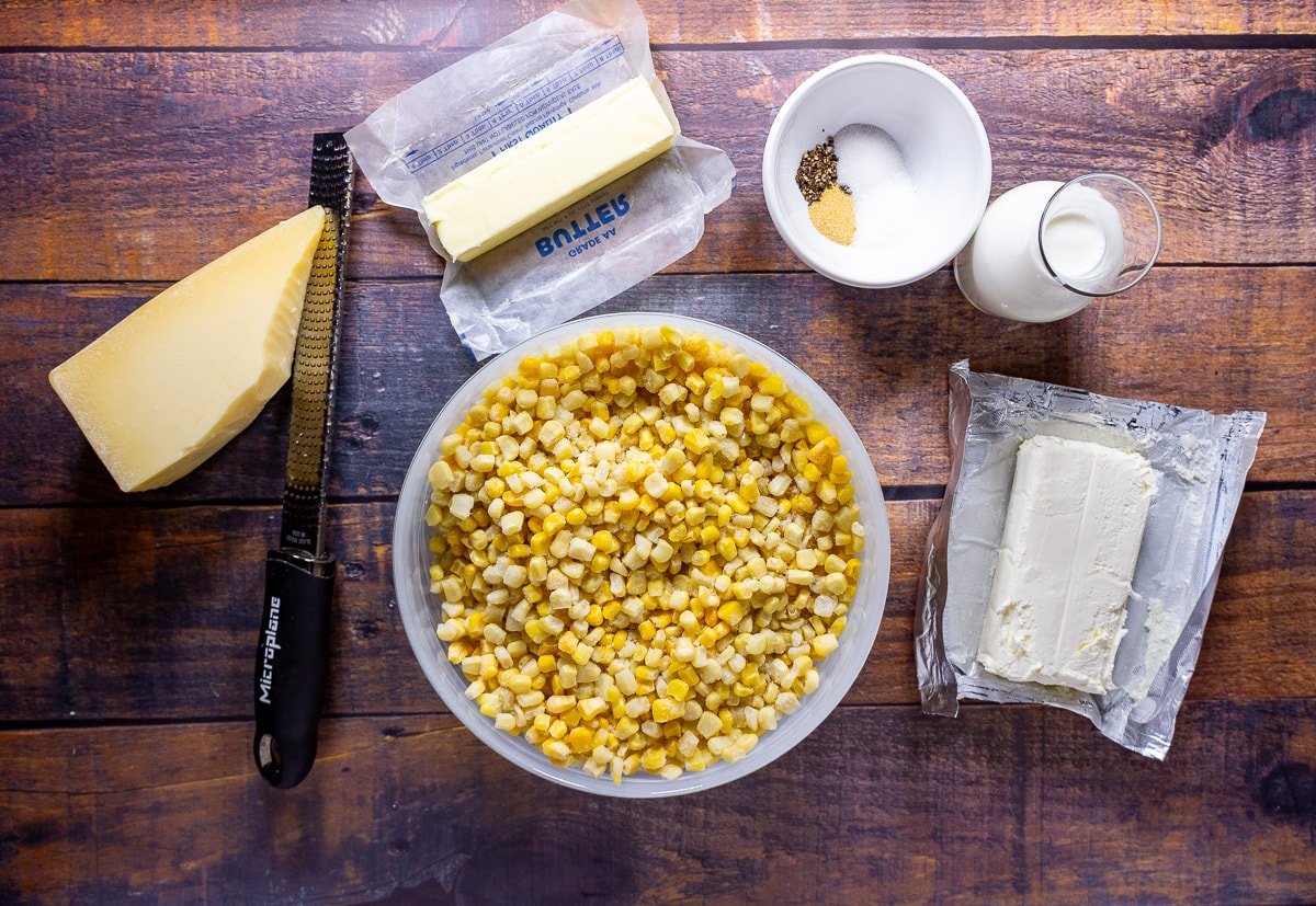 a bowl of corn kernels with parmesan cheese, cream cheese, milk, and butter beside it.