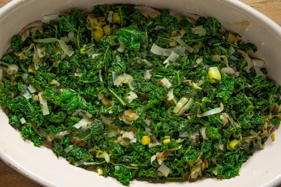 a 9 by 13 baking dish with potatoes topped with kale and leeks