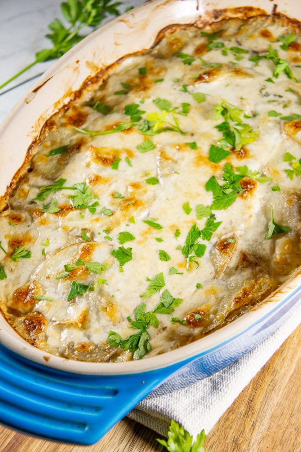 a 9x13 casserole dish with creamy scalloped potatoes that's golden brown on the top and chopped parsley