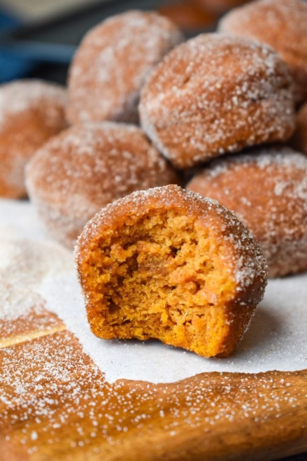a small pile of pumpkin churro mini muffins with one in front with a bite gone on a wooden cutting board