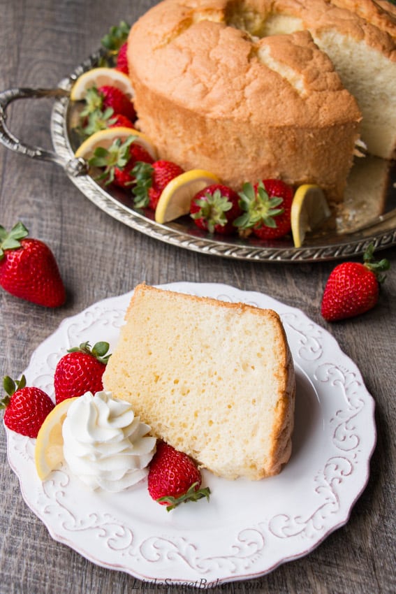 a slice of classic chiffon cake on a metal round platterwhite plate with strawberries in front of the rest of the cake on