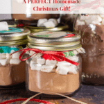 small mason jars of hot cocoa mix with marshmallows on top tied with bows and holiday fabric