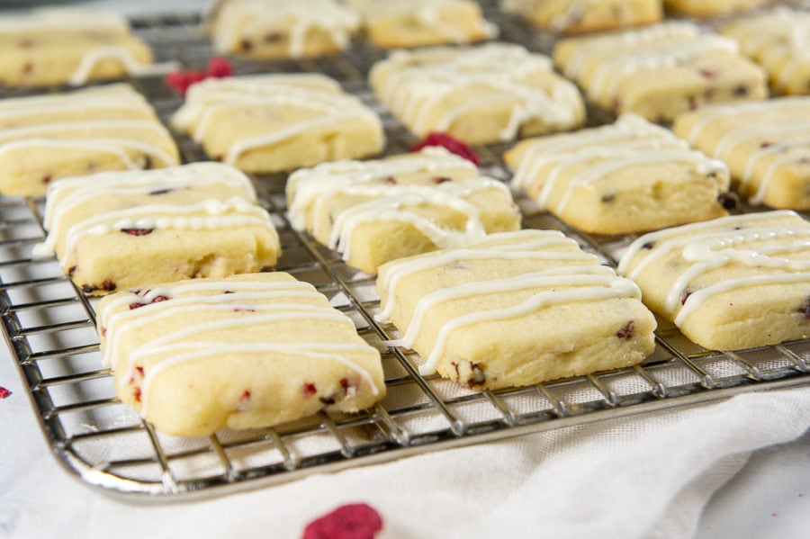 a metal cooling rack with white chocolate raspberry cookies and dried raspberries around it