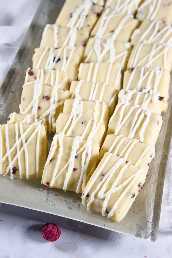 A grey rectangular platter with rows of shortbread cookies with white chocolate and freeze dried raspberries