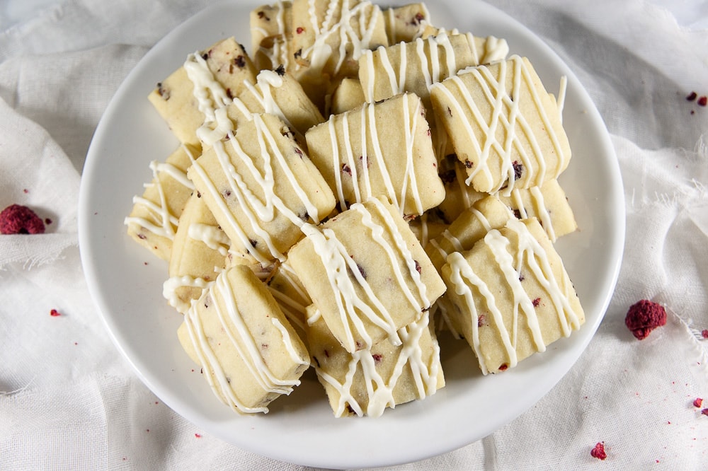 a white bowl of raspberry shortbread cookies drizzled with chocolate