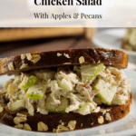a chicken salad sandwich with pecans and apples on a white plate on a wood table