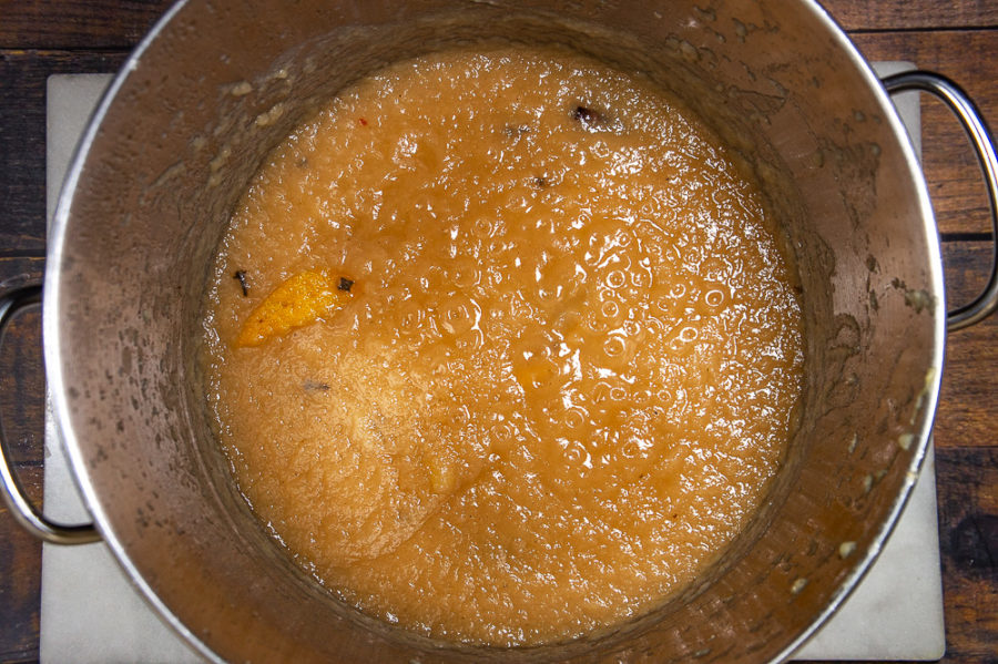 A large steel pot containing cooked pear butter on top of a granite slab on a wooden table