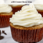 A brown lined spice cupcake with white cream cheese frosting on a granite table with other cupcakes behind it