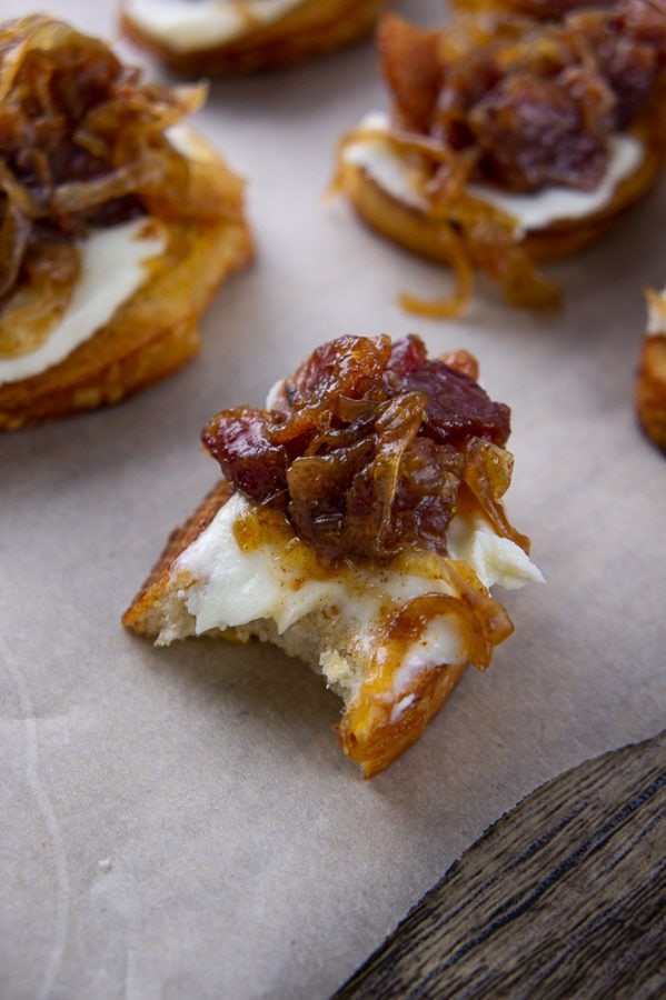 a bacon jam crostini with a bite taken out of it on a parchment paper with other crostinis around it.