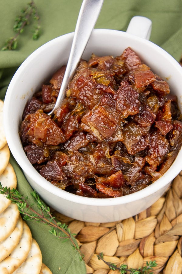 a white bowl of maple bacon onion jam on a tweed placemat beside a green napkin with fresh thyme