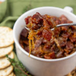 a white bowl of maple bacon onion jam with a fork lifting a bite out of it