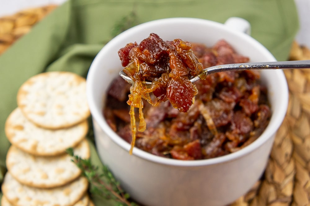 a white bowl of maple bacon onion jam with a fork lifting a bite out of it