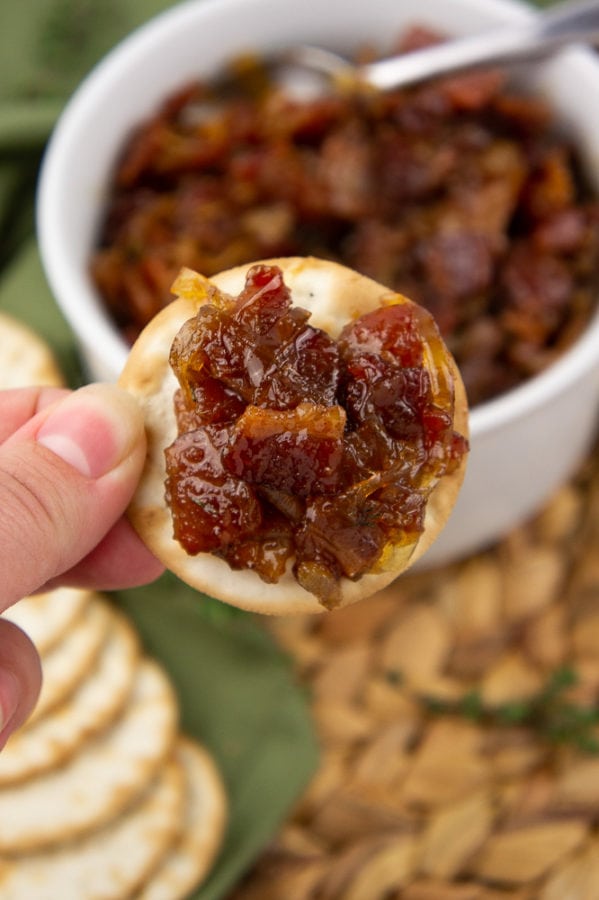 cracker with bacon jam held over a white bowl full of bacon jam