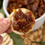 a cracker topped with bacon and onion jam held above a white bowl of jam