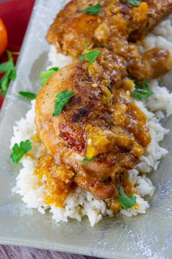 a platter of white rice topped with braised chicken thighs and an orange sauce with chopped parsley