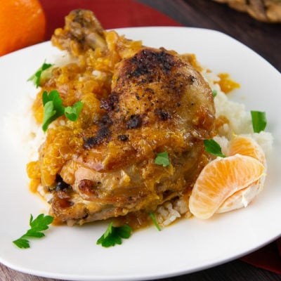 a chicken thigh braised with oranges over rice with parsley on a white plate