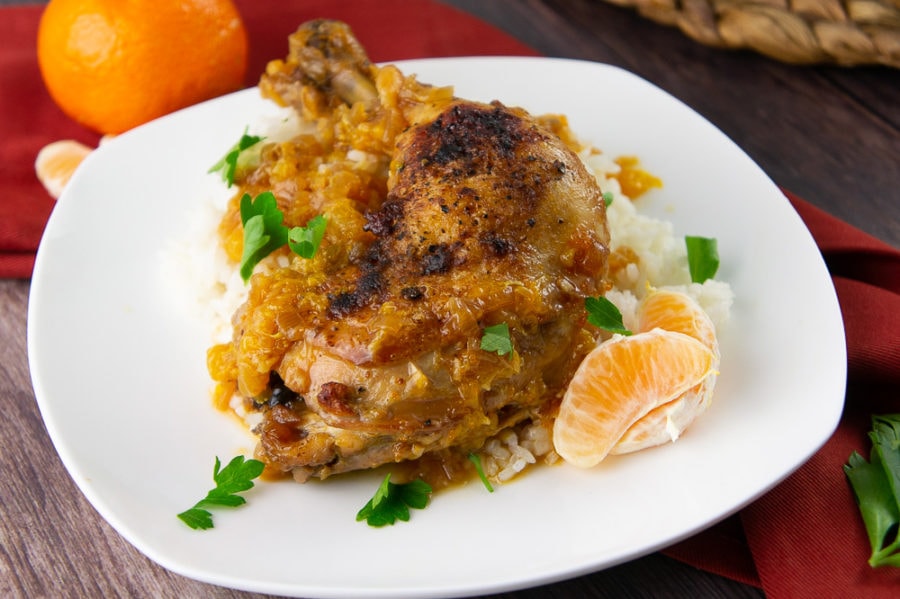 a chicken thigh braised with oranges over rice with parsley on a white plate