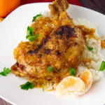 braised chicken with orange sauce on a white plate over rice with chopped parsley