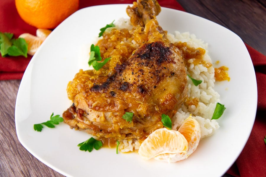 braised chicken with orange sauce on a white plate over rice with chopped parsley