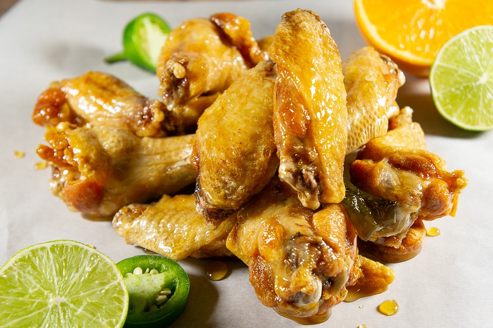 tequila lime chicken wings on a parchment sheet with sliced limes and oranges