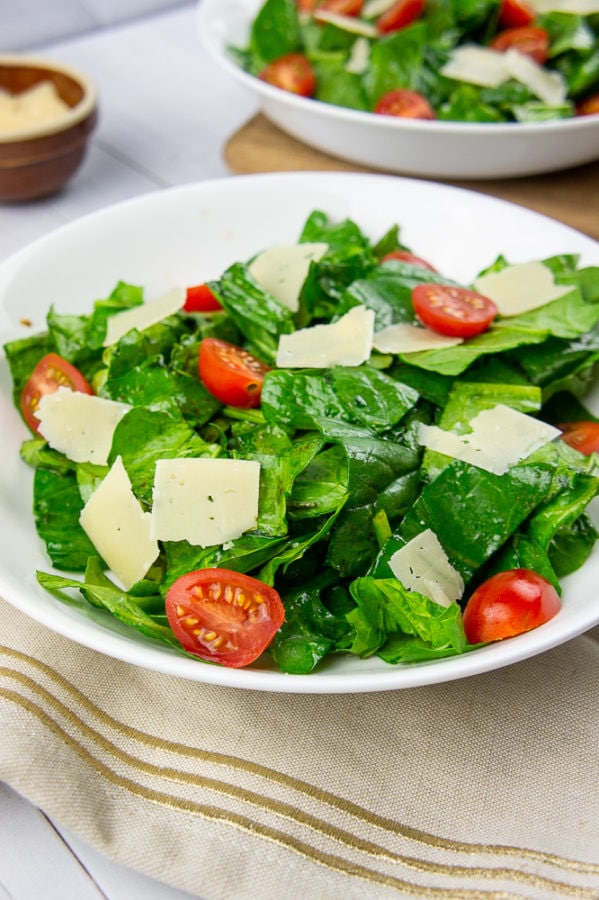 a bowl of tomato spinach salad with parmesan on a beige towel