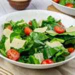 a bowl of tomato spinach salad with parmesan on a beige towel