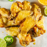 a pile of deep fried chicken wings with a glaze surrounded by jalapeno slices and citrus fruits.