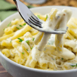 A fork with creamy sauced noodles on it over a bowl of pasta