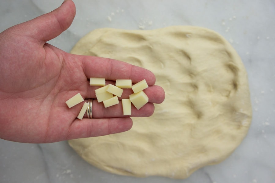 asiago bread dough flattened with a hand holding chunks of cheese above it.