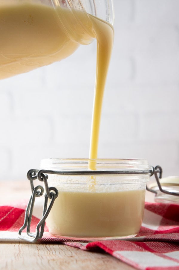 a mason jar pouring condensed milk into a smaller jar on a red checked napkin