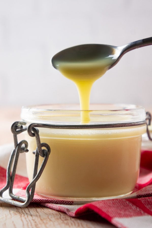 a glass jar with sweetened condensed milk, a spoon held above it, drizzling it back in.