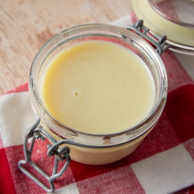 a glass jar of homemade sweetened condensed milk on a red and white checked napkin