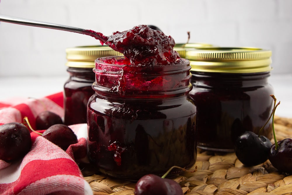 a jar of cherry vanilla jam with a spoon scooping some out