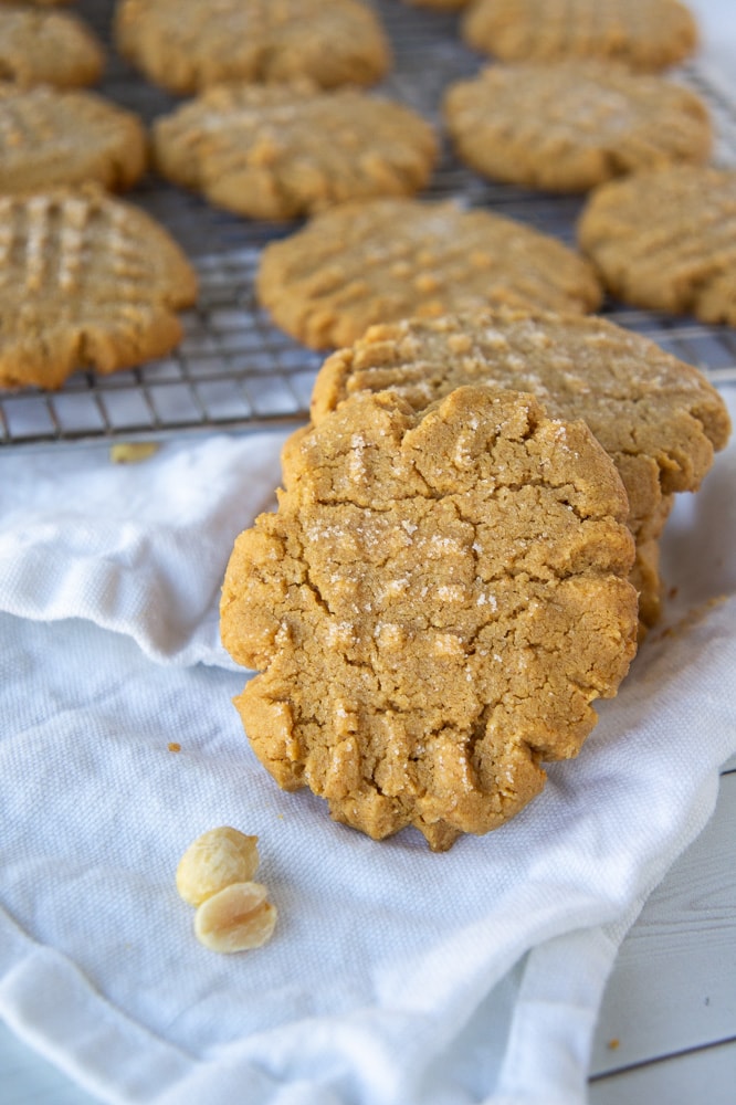 a stack of flourless peanut butter cookies in front of a cooling rack of cookies