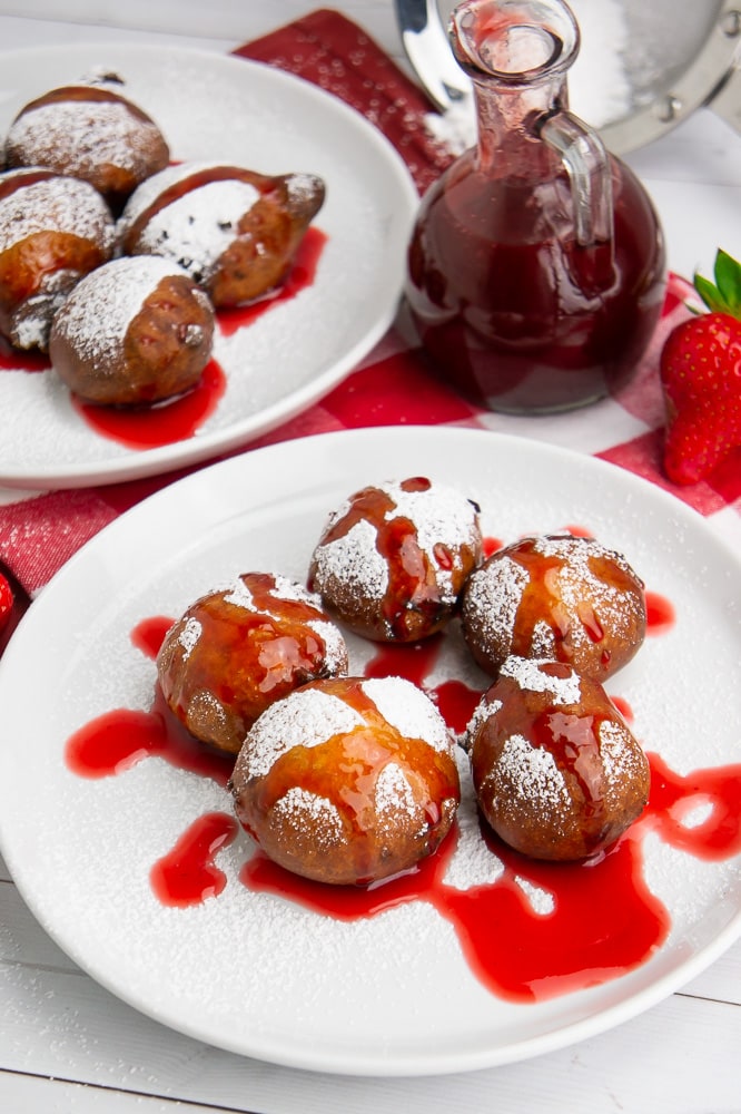 fried cheesecake bites topped with powdered sugar and strawberry syrup on a white plate