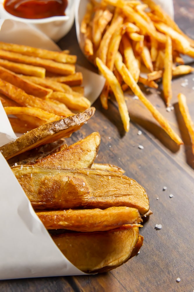 three white parchment cones with three different cuts of french fries on a wooden table