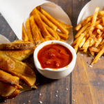 three cones of fries with ketchup on a wooden table